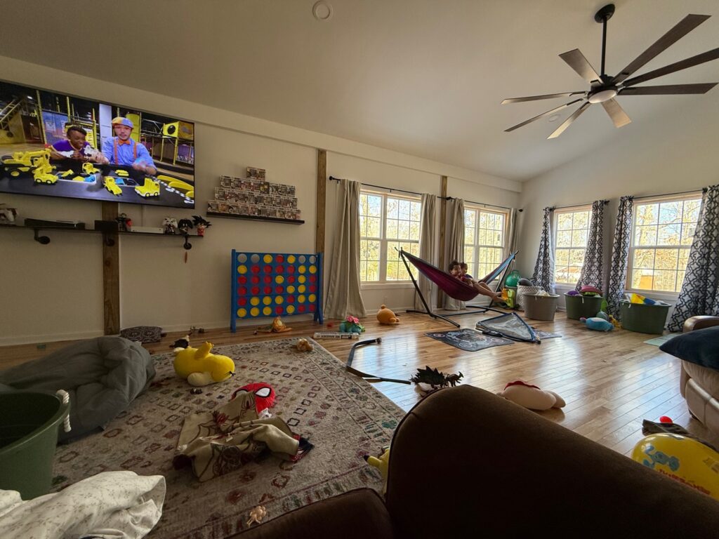 Living room covered in toys, with children swinging in a hammock in front of windows